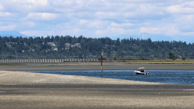 A boat traverses a narrow strip of water during low tide.